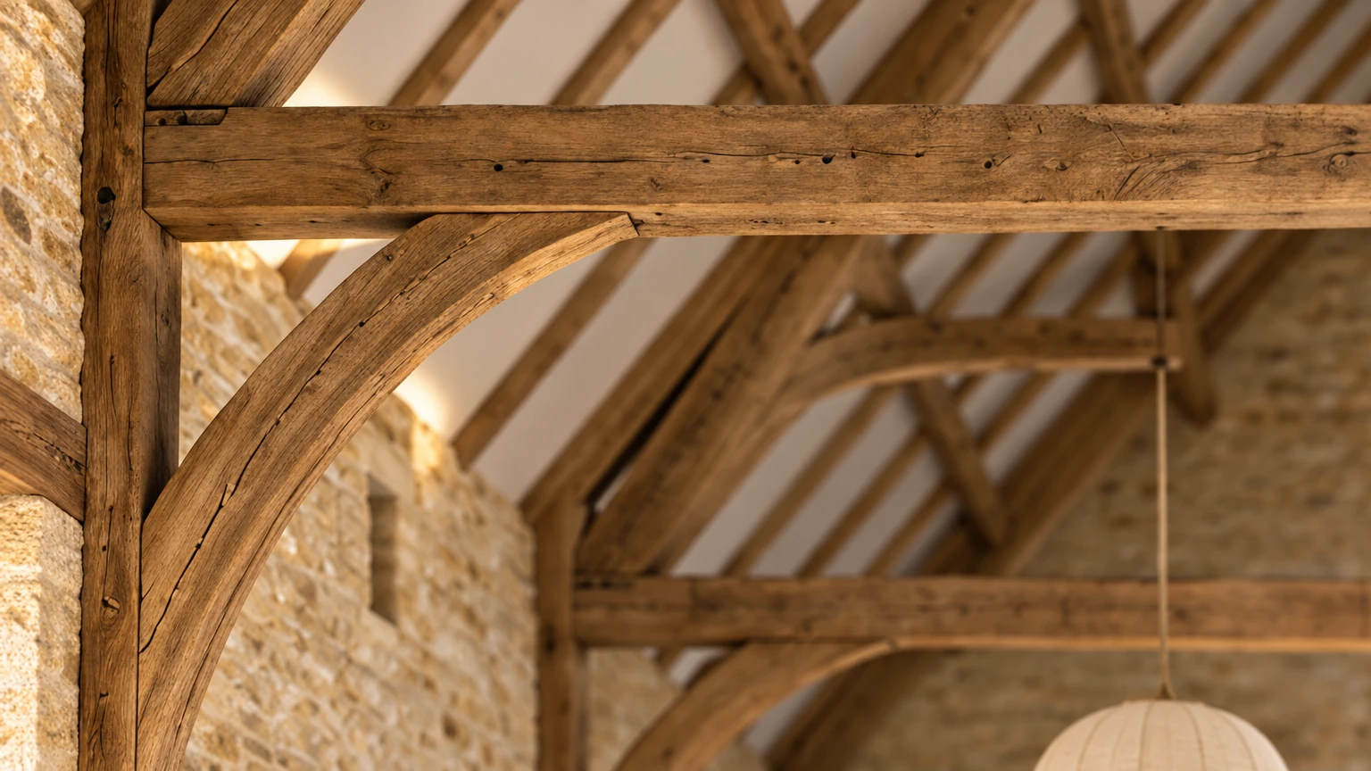 AI-generated Concept detail of a pegged oak tie-beam meeting a post and curved wind-brace, with honey-stone walls, a glazed slit and a paper pendant below.