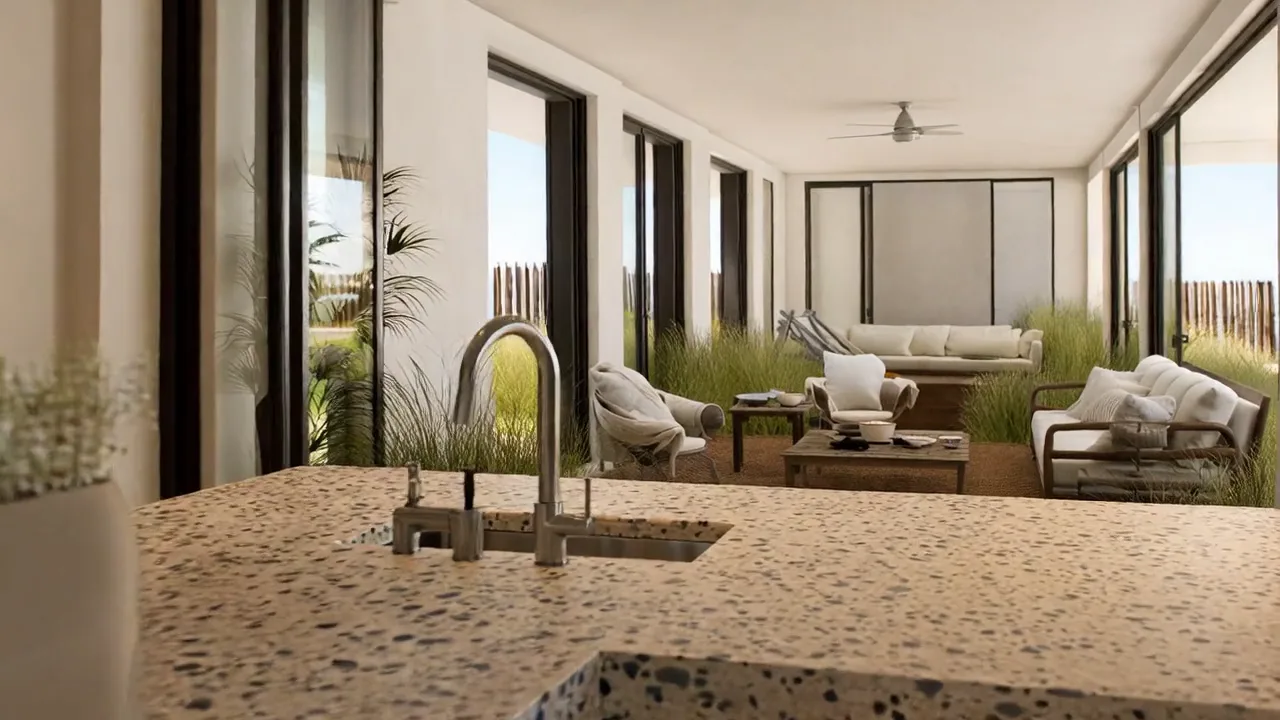 Terrazzo kitchen island and brushed-steel tap in the foreground, with a long shaded living veranda, lounge chairs and coastal grasses beyond tall glazed openings.