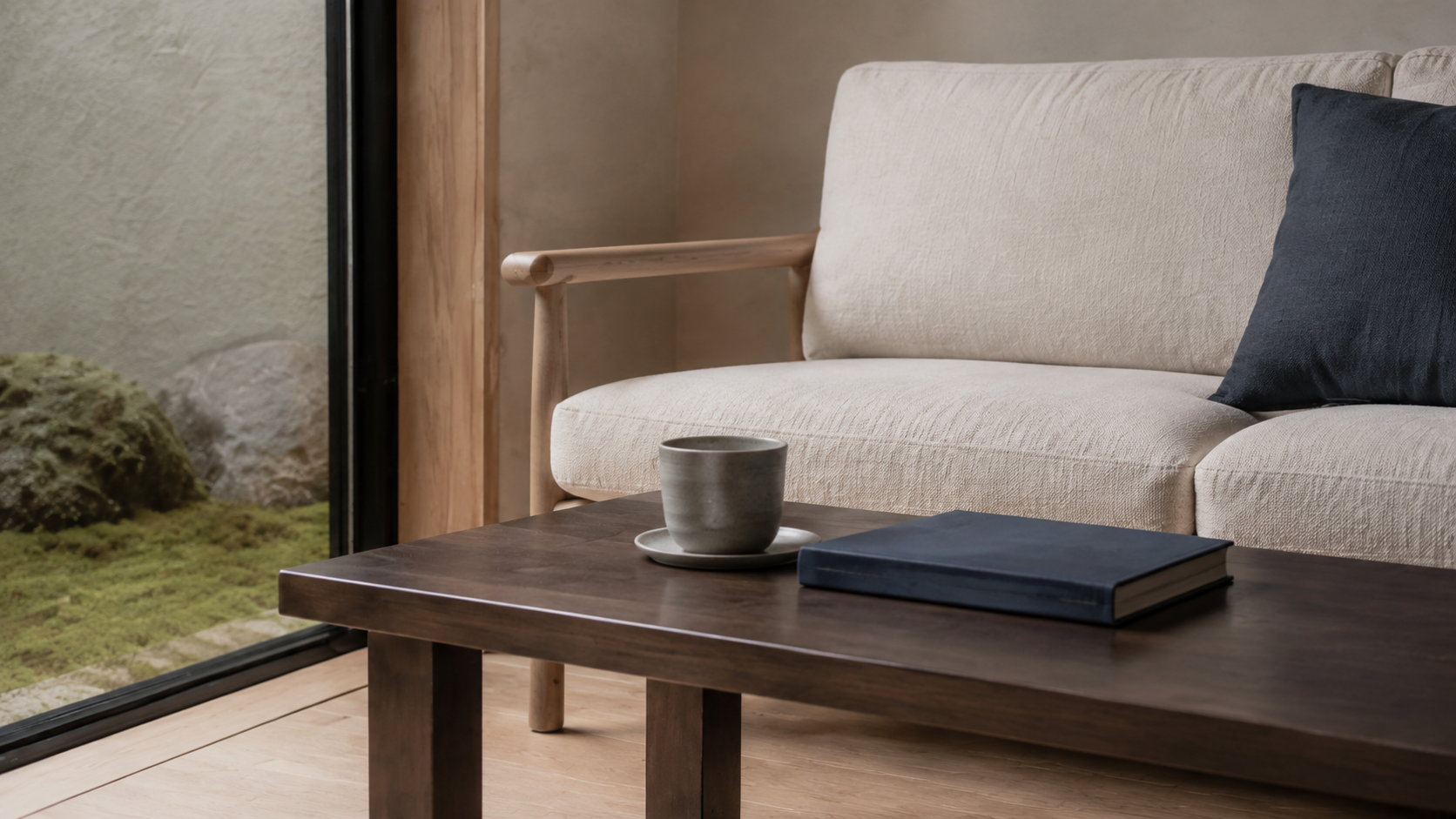 AI-generated Concept close view of an ivory sofa arm and dark timber coffee table with one grey cup, saucer and closed indigo book.